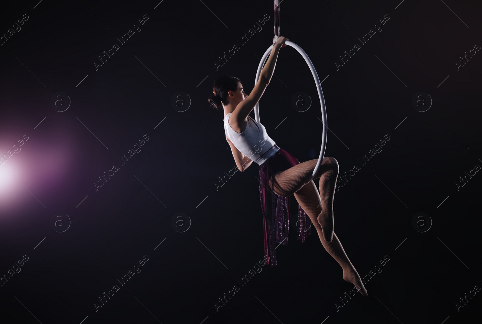 Photo of Young woman performing acrobatic element on aerial ring against dark background. Space for text