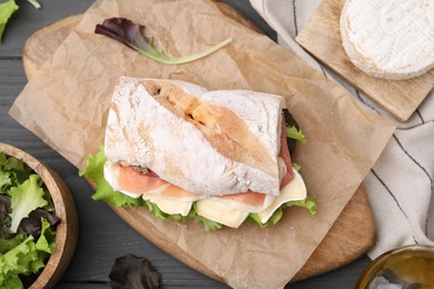 Tasty sandwich with brie cheese and prosciutto on grey wooden table, flat lay