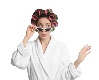 Photo of Emotional young woman in bathrobe with hair curlers and sunglasses on white background