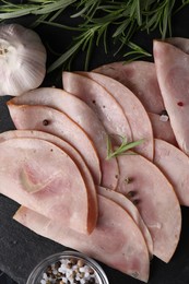 Photo of Tasty ham with rosemary, garlic, sea salt and peppercorns on black board, flat lay
