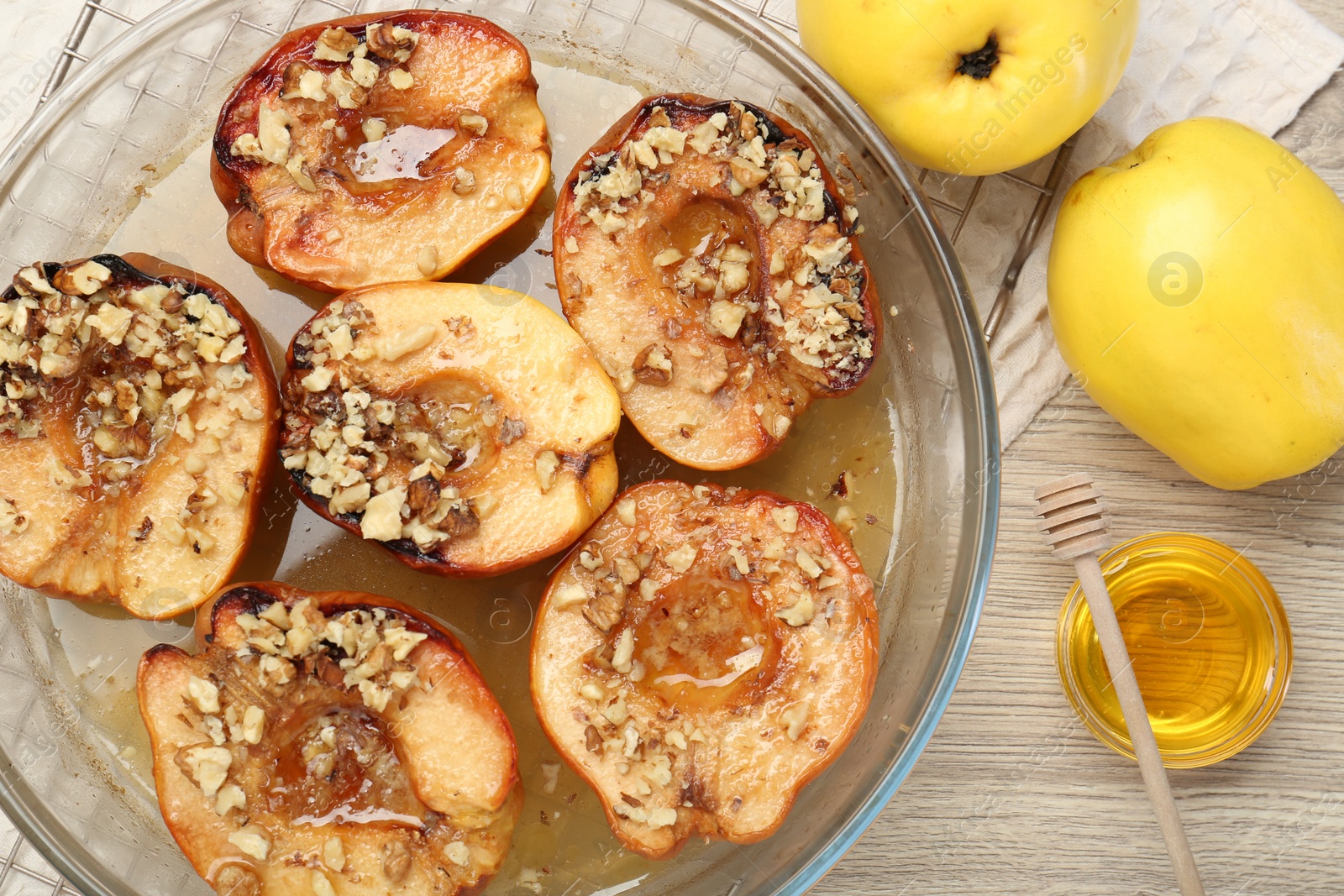 Photo of Delicious baked quinces with nuts in bowl, honey and fresh fruits on wooden table, flat lay