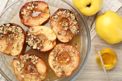 Delicious baked quinces with nuts in bowl, honey and fresh fruits on wooden table, flat lay