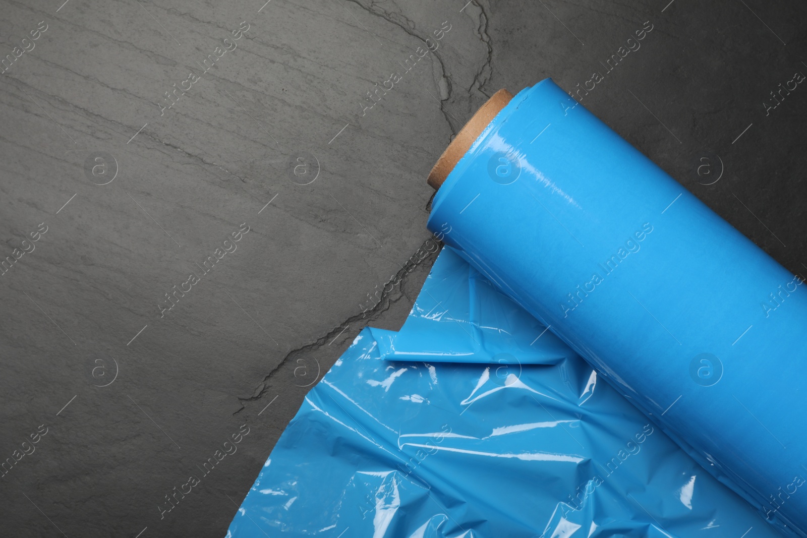 Photo of Roll of plastic stretch wrap film on black table, top view. Space for text