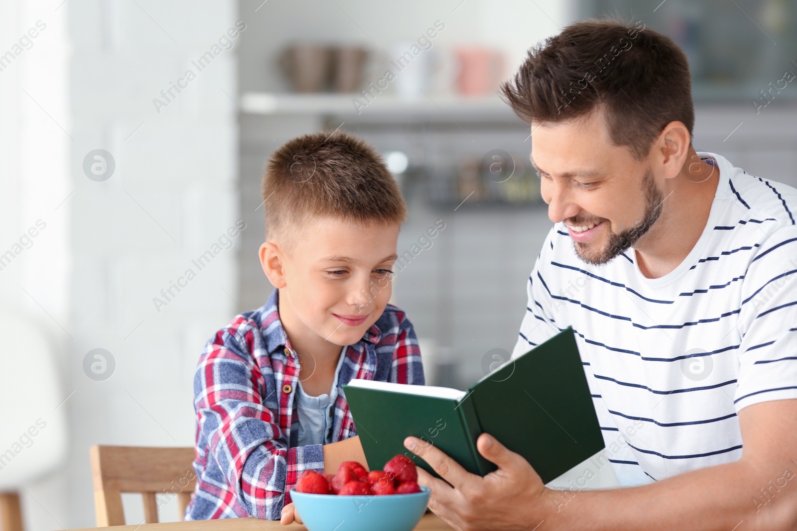 Photo of Dad and son reading interesting book in kitchen