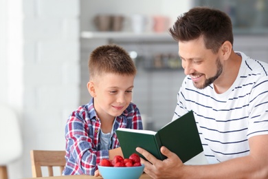 Dad and son reading interesting book in kitchen