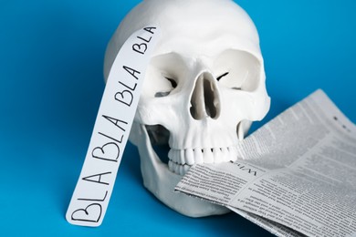 Information warfare concept. Useless nonsense in mind as result of media propaganda influence. Human skull with newspaper on light blue background, closeup