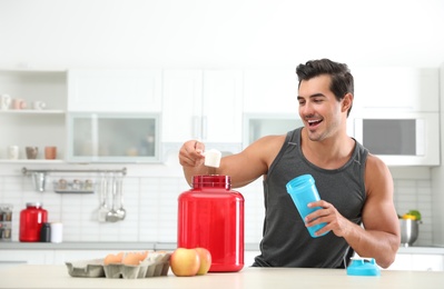 Young athletic man preparing protein shake in kitchen, space for text