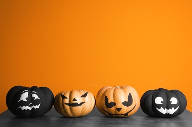 Photo of Pumpkins with scary faces on table against color background, space for text. Halloween decor