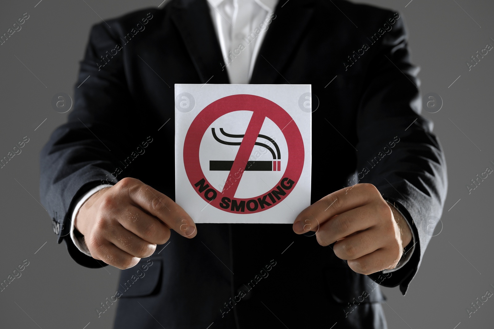 Photo of Man holding card with no smoking sign on gray background, closeup