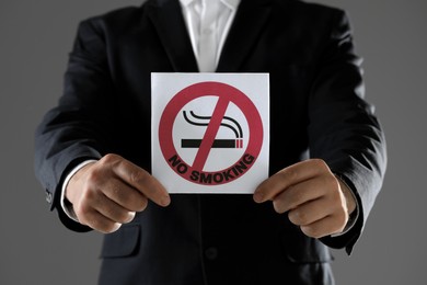 Photo of Man holding card with no smoking sign on gray background, closeup