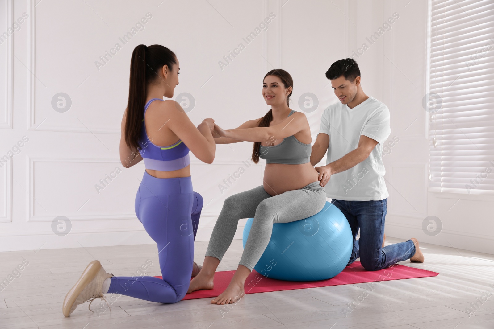 Photo of Pregnant woman and her husband working with trainer in gym. Preparation for child birth