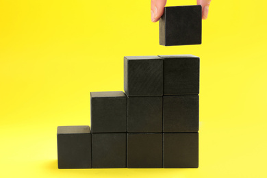 Woman building steps of wooden cubes on yellow background, closeup. Career promotion concept