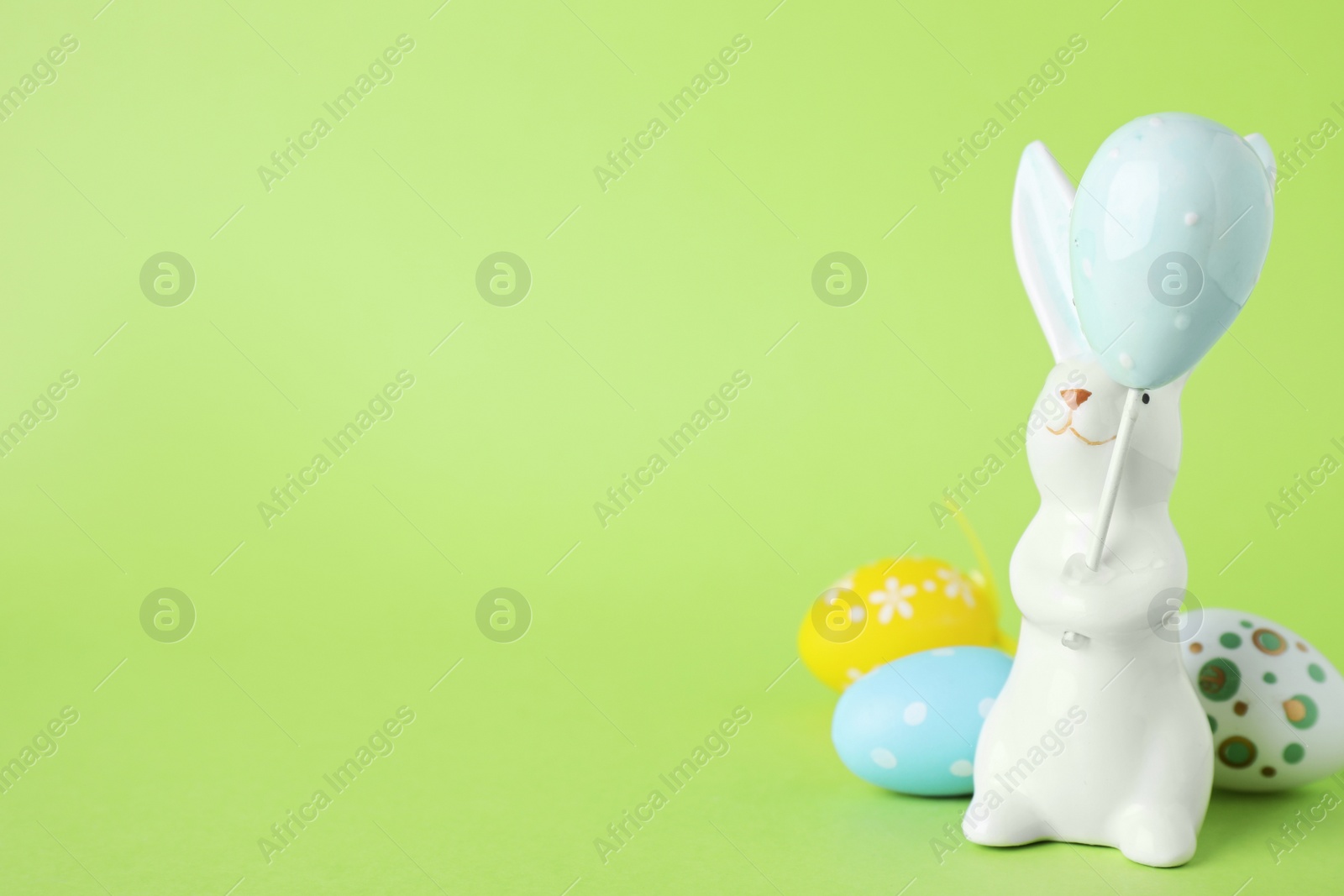 Photo of Easter bunny figure and dyed eggs on green background. Space for text