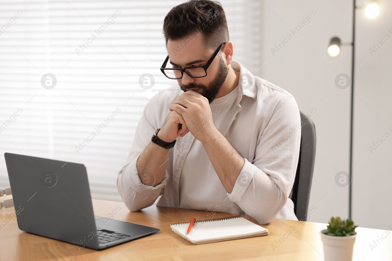 Photo of Young man in glasses watching webinar at table in room