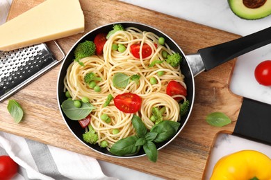 Photo of Delicious pasta primavera in frying pan and ingredients on white table, flat lay