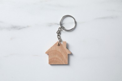 Wooden keychain in shape of house on marble table, top view