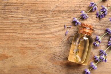 Bottle of essential oil and lavender flowers on wooden table, flat lay. Space for text