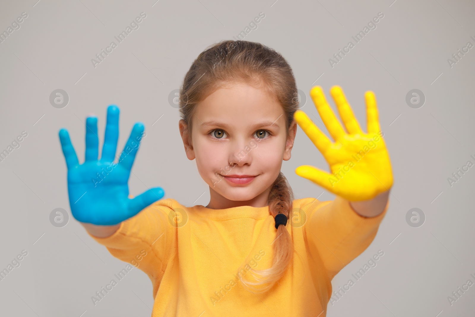 Photo of Little girl with hands painted in Ukrainian flag colors on light grey background. Love Ukraine concept