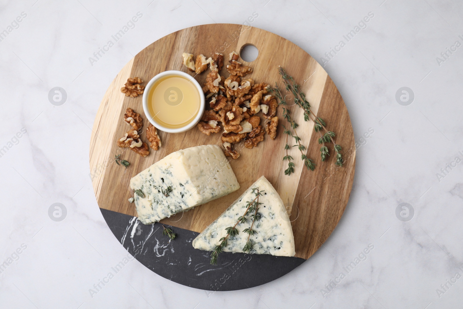 Photo of Tasty blue cheese with thyme, honey and walnuts on white marble table, top view