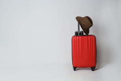 Photo of Travel suitcase with hat and camera on light grey background, space for text. Summer vacation