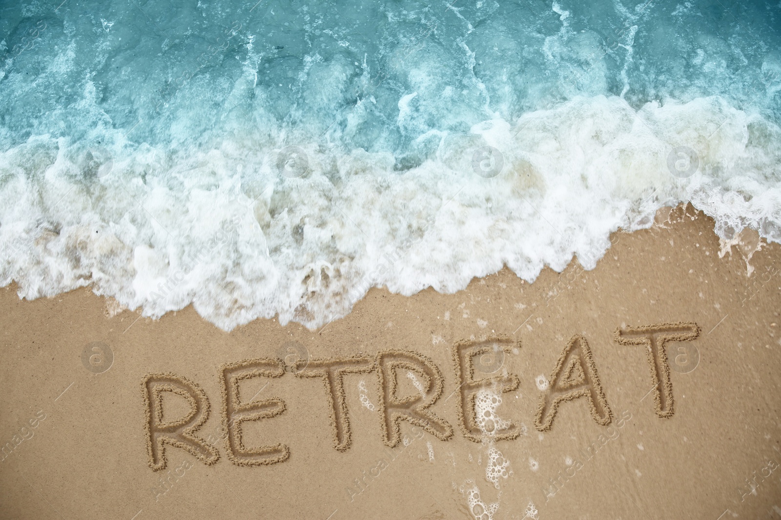 Image of Word Retreat drawn on sand near sea, above view