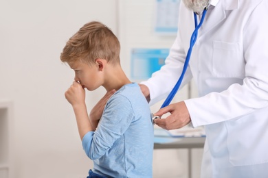 Doctor examining coughing little boy at clinic