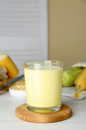Tasty fresh corn milk in glass on white wooden table