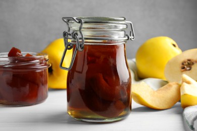 Photo of Tasty homemade quince jam in jars and fruits on white wooden table, closeup