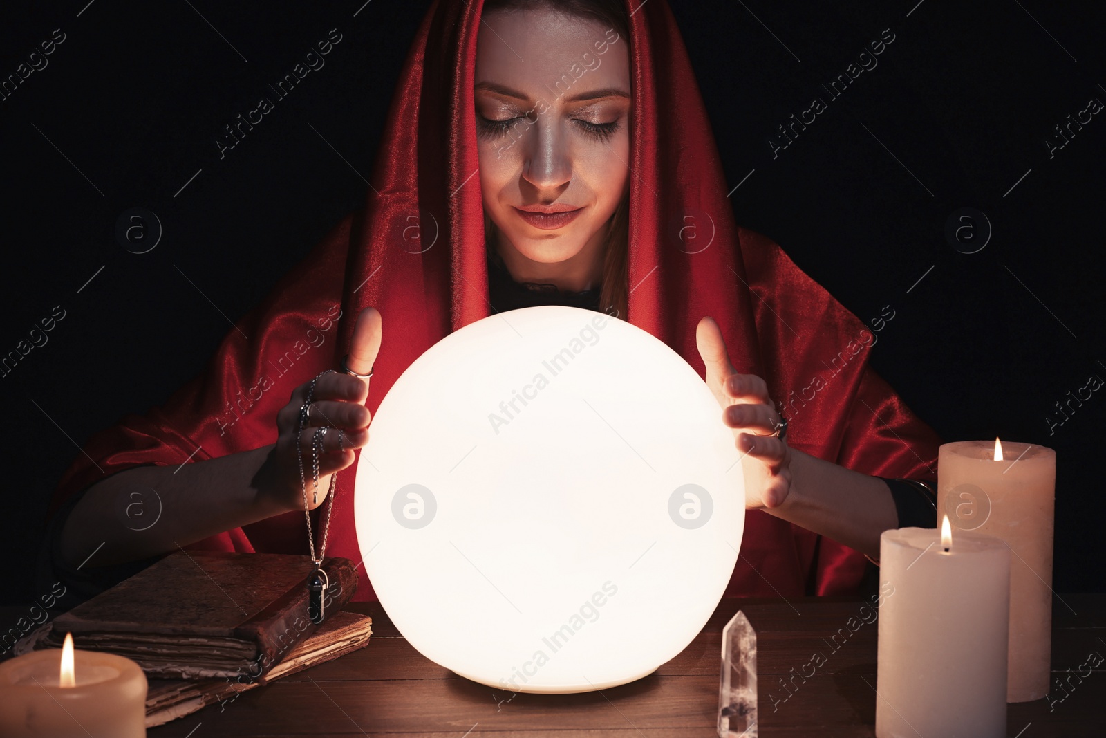 Photo of Soothsayer using glowing crystal ball to predict future at table in darkness. Fortune telling