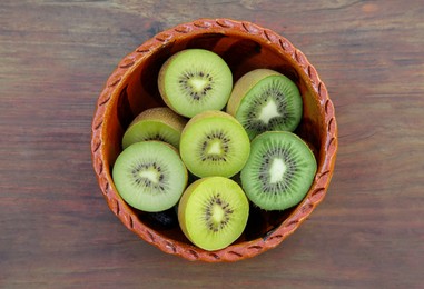 Photo of Bowl of many cut fresh kiwis on wooden table, top view