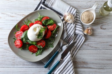 Delicious burrata cheese served with tomatoes and basil on white wooden table, flat lay