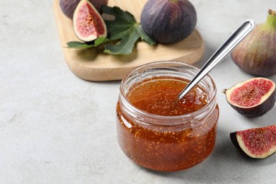Jar with tasty fig jam and fresh fruits on white table, closeup. Space for text