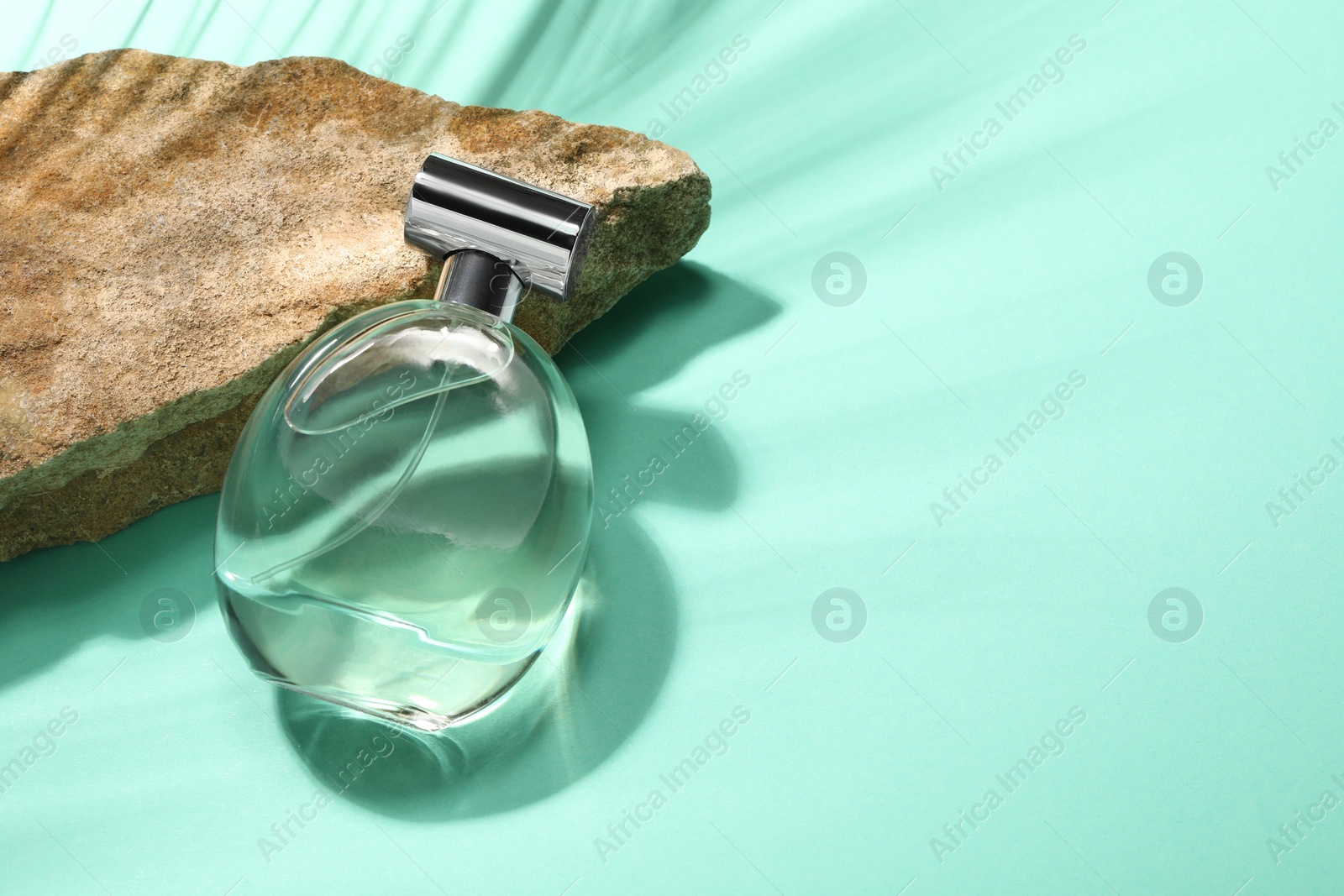 Photo of Bottle of luxury perfume in sunlight and stone on turquoise background, above view. Space for text