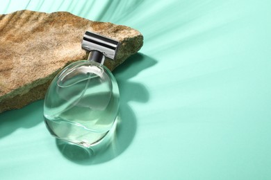 Bottle of luxury perfume in sunlight and stone on turquoise background, above view. Space for text