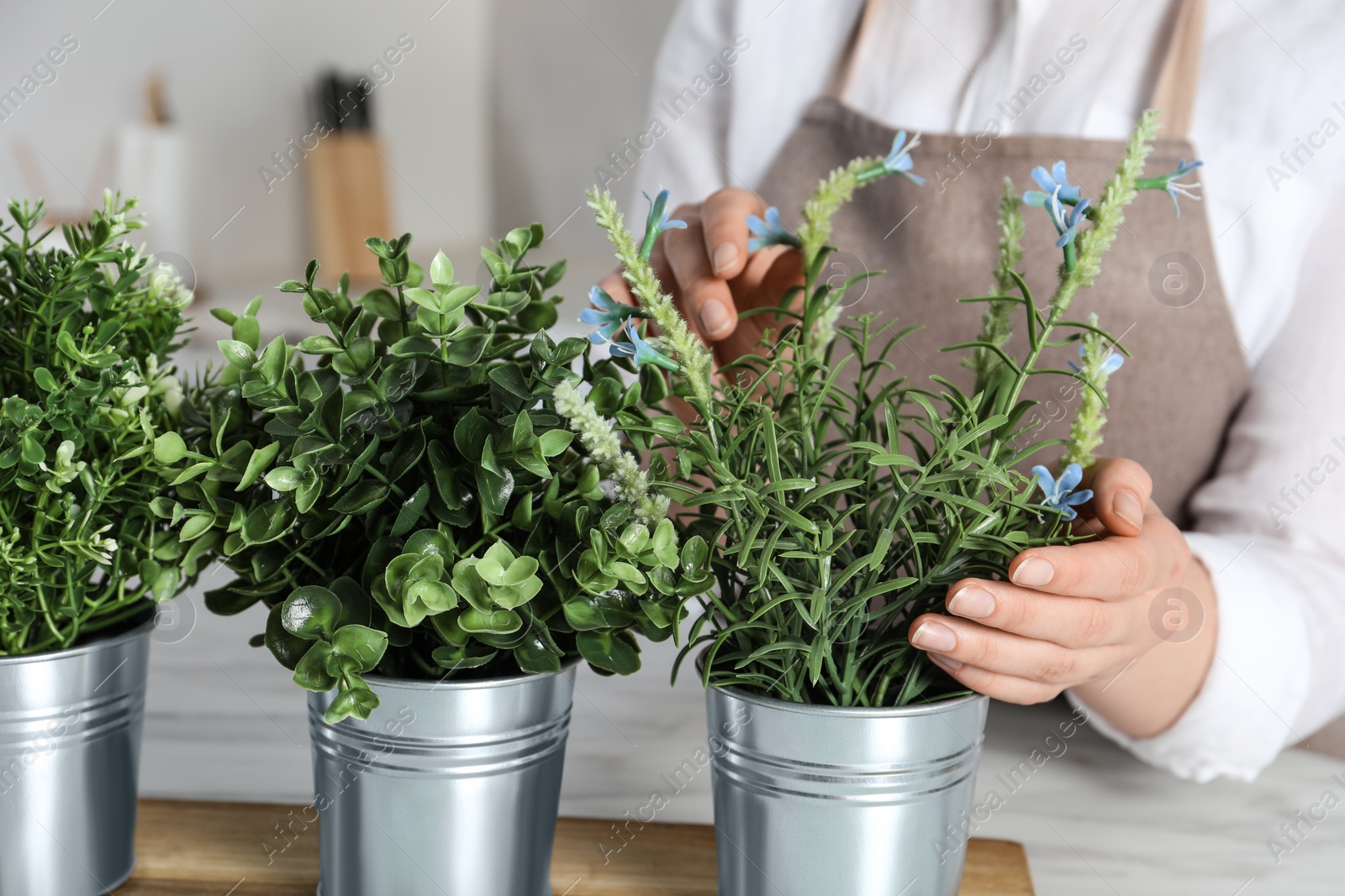 Photo of Woman near white marble table with different artificial potted herbs in kitchen, closeup