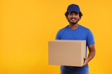 Photo of Happy courier with parcel on orange background, space for text