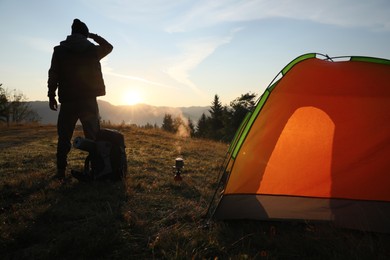 Man with backpack near camping tent at sunset, back view