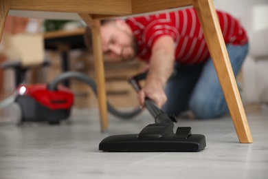 Photo of Young man using vacuum cleaner at home, focus on nozzle