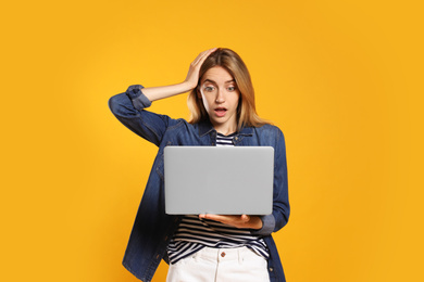 Portrait of emotional woman with modern laptop on yellow background