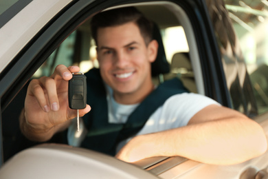 Happy man sitting in modern car at dealership, focus on hand with key
