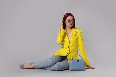 Photo of Stylish woman with red dyed hair and bag sitting on light gray background