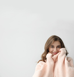 Photo of Beautiful young woman wearing warm pink sweater on light background. Space for text