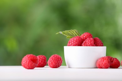 Tasty ripe raspberries and green leaf on white table outdoors. Space for text