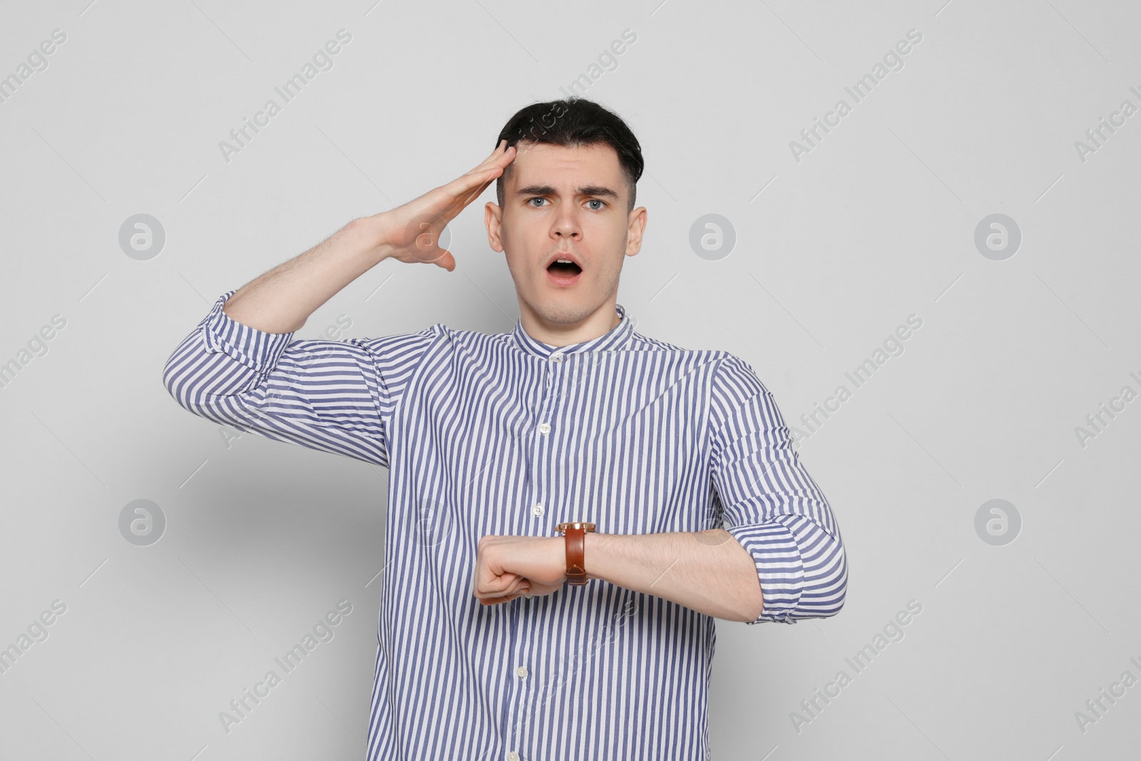 Photo of Emotional young man checking time on light grey background. Being late concept