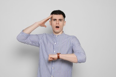 Emotional young man checking time on light grey background. Being late concept