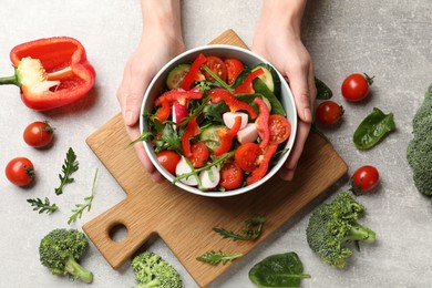 Woman with tasty fresh vegetarian salad at light grey table, top view