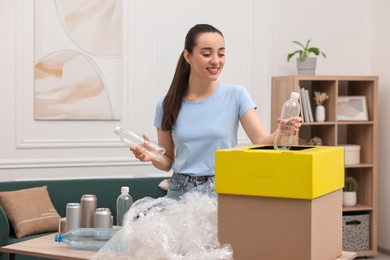 Garbage sorting. Smiling woman throwing plastic bottle into cardboard box in room