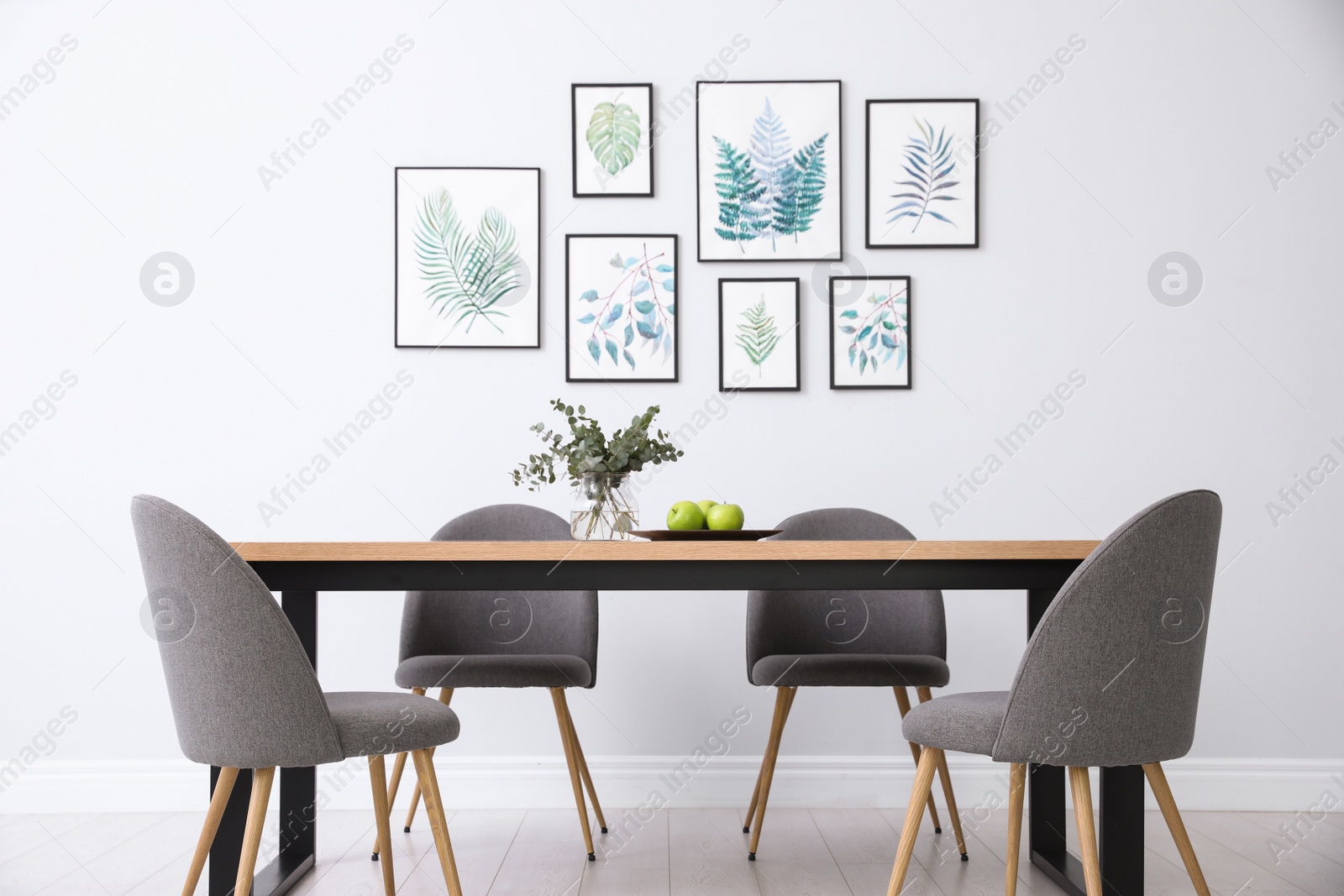 Photo of Stylish room interior with modern table, chairs and paintings of tropical leaves. Idea for design