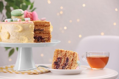 Delicious cake and tea served on white table against blurred lights