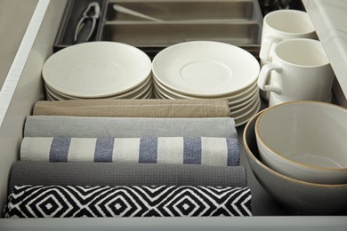 Photo of Open drawer of kitchen cabinet with different dishware and towels, closeup